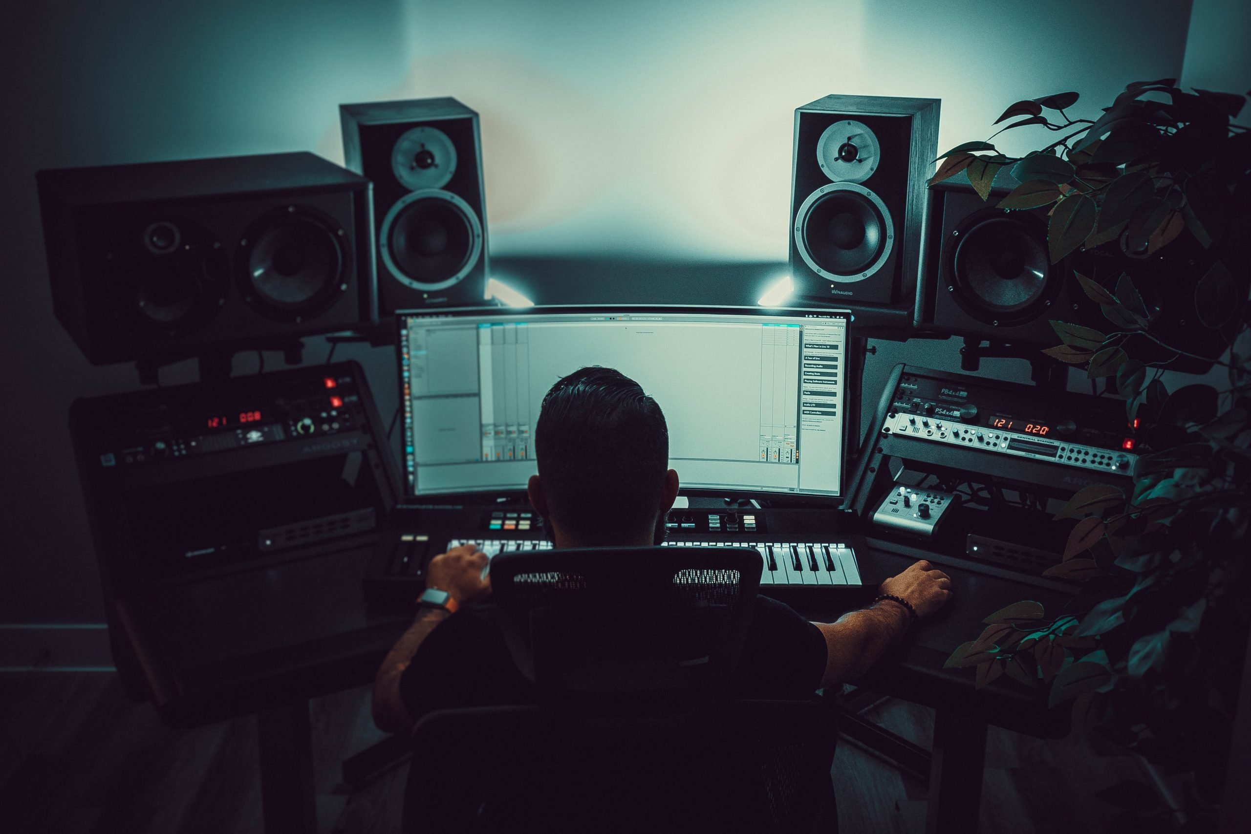 A young man producing music in his bedroom studio, surrounded by a MIDI keyboard, headphones, and a computer running a DAW (Digital Audio Workstation)